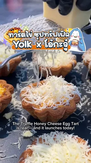 ภาพถ่ายระยะใกล้ของทาร์ตไข่ทรัฟเฟิลฮันนี่ชีสสีทองอร่าม ที่มีชีสขูดสีเหลืองทองละลายเยิ้มปกคลุมอยู่ด้านบนอย่างหนาแน่น มองเห็นขอบทาร์ตกรอบสวยงาม ด้านในคาดว่ามีไส้ซอสทรัฟเฟิลและน้ำผึ้งผสมผสานกันอย่างลงตัว ทาร์ตนี้เป็นเมนูพิเศษจากการร่วมมือกันระหว่าง YOLK และ Ohkajhu ในชื่อ "Truffle Honey Cheese Egg Tart" ราคาชิ้นละ 135 บาท มีจำหน่ายตั้งแต่วันที่ 18 สิงหาคม ถึง 31 ตุลาคม 2568 ที่ YOLK ทุกสาขา รวมถึงสาขา Central World ชั้น 7
