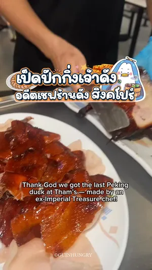 ภาพเป็ดปักกิ่งหนังกรอบสีเหลืองทองกำลังถูกแล่บนโต๊ะโดยเชฟผู้มีประสบการณ์จากร้านดังในสิงคโปร์ ณ ร้าน Tham’s Roasted Delights สาขา Ang Mo Kio Singapore เป็ดปักกิ่งราคา 47 SGD สำหรับทั้งตัวนี้เสิร์ฟพร้อมแป้งสำหรับห่อและน้ำจิ้ม มีบะหมี่เป็ดย่างและผัดผักสดกรอบจัดวางอยู่บนโต๊ะ แสดงถึงมื้ออาหารที่น่ารับประทานในแบบฉบับ hawker ของสิงคโปร์