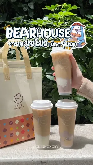 ภาพระยะใกล้ของแก้วชานม "ชานมมูนโมจิเผือกนุ่ม" เมนูใหม่ล่าสุดจาก BEARHOUSE เครื่องดื่มสีน้ำตาลอ่อนในแก้วพลาสติกใส มีท็อปปิ้งโมจิข้าวไทยสีขาวอุ่นทรงกลมหนึบหนับลอยอยู่ด้านบน และชิ้นเผือกนุ่มสีม่วงอ่อนจากเมืองกาญจน์ด้านล่าง มีหลอดสีดำปักอยู่ บนแก้วมีโลโก้ BEARHOUSE และข้อความ "Happiness Every Day"
